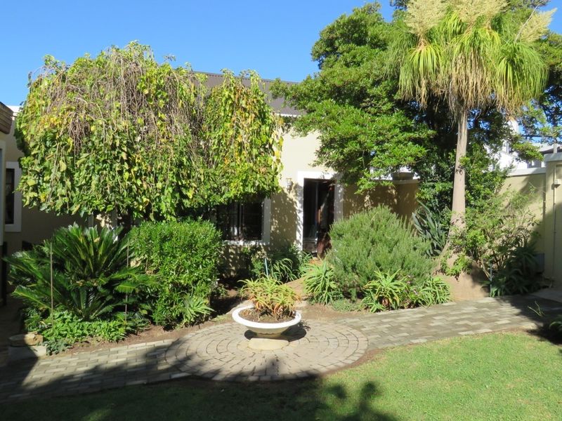 A well-maintained rear garden area featuring a paved circular walkway, established landscaping, and a secure wrought iron gate.