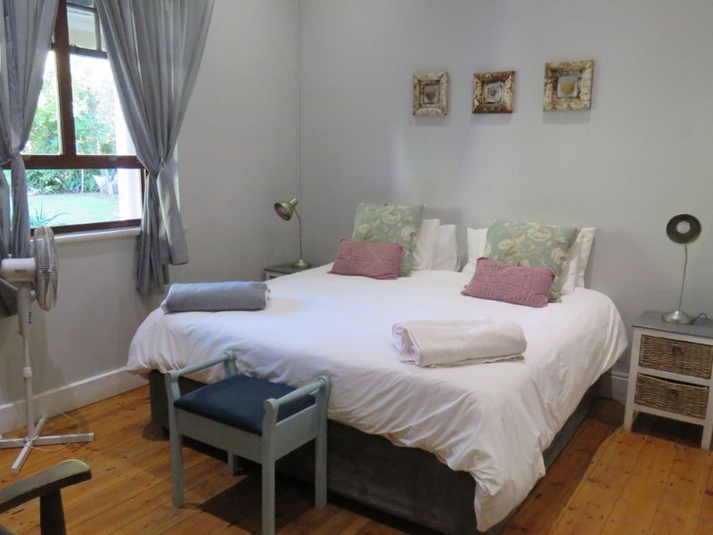 A bedroom featuring polished timber flooring, neutral walls, and a window with garden views.