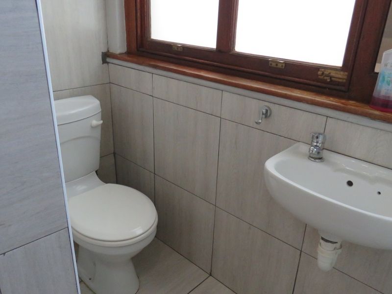A compact bathroom featuring tiled walls and flooring, a wall-mounted basin with a mixer tap, and a standard toilet.