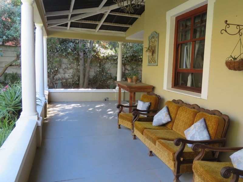 A covered patio area featuring concrete columns, exposed roof rafters, and a timber window frame overlooking a garden space.