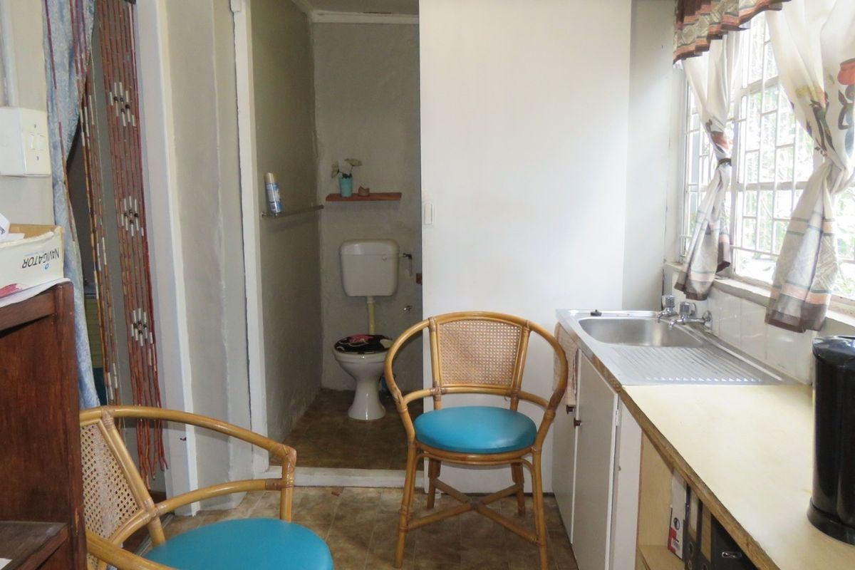 A compact kitchen area featuring a stainless steel sink, laminate countertop, and built-in cabinetry, with an adjacent small bathroom facility.