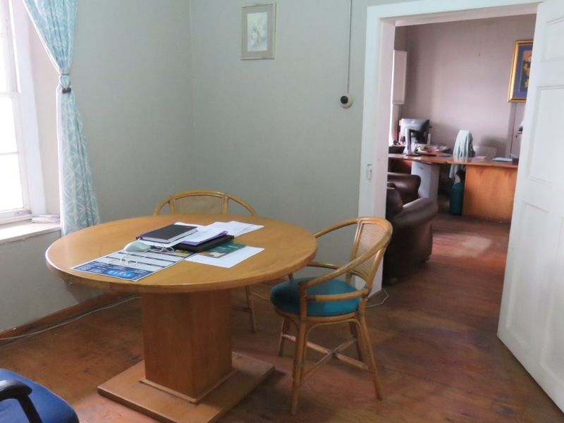 A functional office space featuring timber flooring, a sash window, and an open doorway leading to an adjacent workspace.