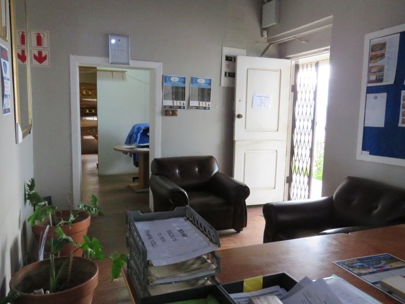 A functional office space featuring a security gate, internal door access, and visible electrical distribution board, suitable for a professional business environment.