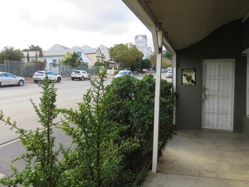 A covered veranda entrance area featuring a security gate and concrete flooring, overlooking a street-side view.