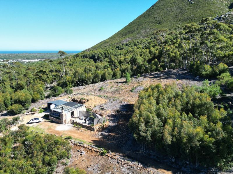 Aerial view of a small holding property nestled against a mountain slope, featuring a dwelling with a metal roof and stone accents.