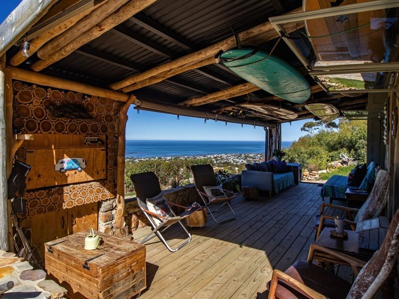 A rustic covered patio featuring timber decking, exposed log beams, and a stone wall, offering expansive coastal and landscape views.