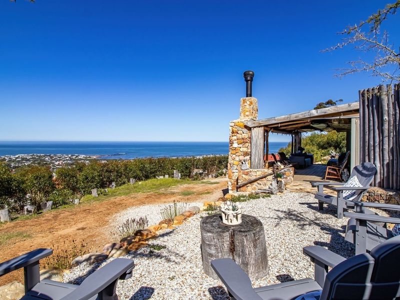 Outdoor entertainment area featuring a stone fireplace and timber structure, offering expansive coastal views over the surrounding landscape.