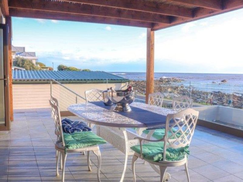 Covered outdoor patio featuring tiled flooring, a timber pergola, and a glass balustrade with direct ocean views.