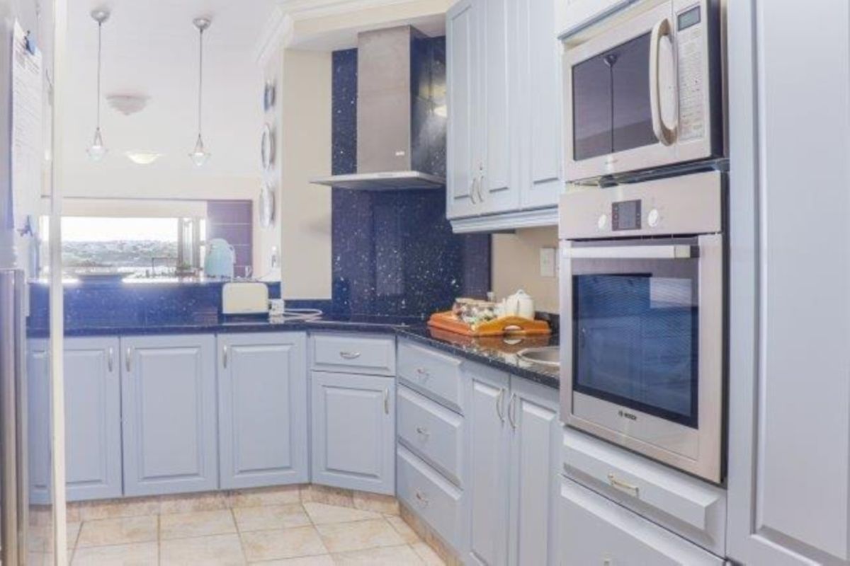 A functional kitchen featuring light blue cabinetry, dark granite countertops, tiled flooring, and integrated stainless steel appliances including an oven and microwave.