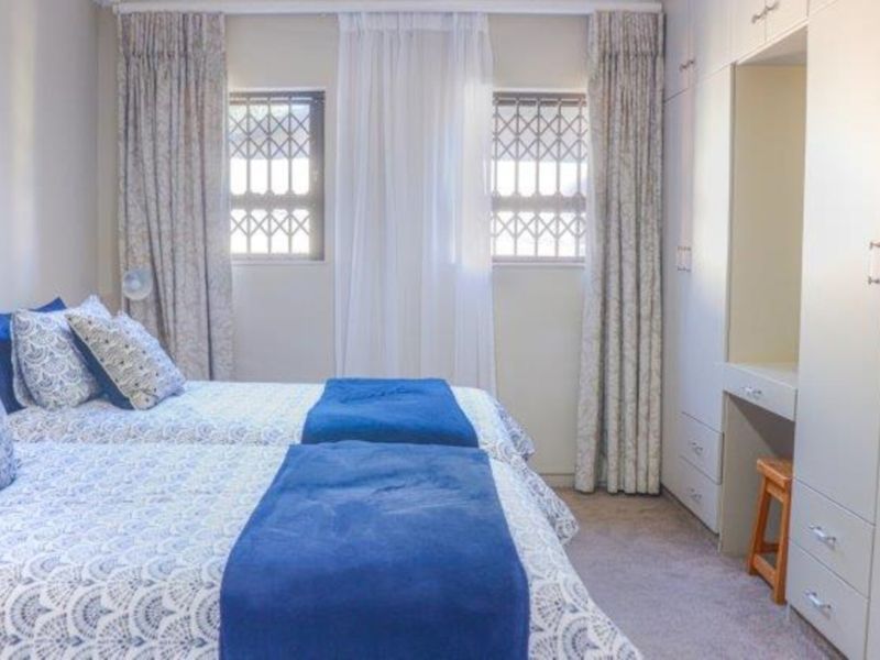 A well-maintained bedroom featuring built-in cupboards with an integrated vanity area, carpeted flooring, and windows fitted with security bars.
