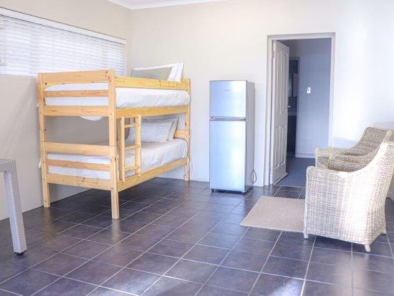 A functional bedroom featuring dark tiled flooring and venetian blinds, providing a neutral space with direct access to an adjoining room.