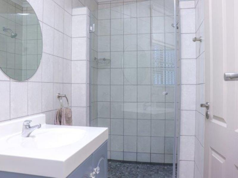 A clean, functional bathroom featuring a vanity with a basin, a glass-enclosed shower, and neutral wall tiling.