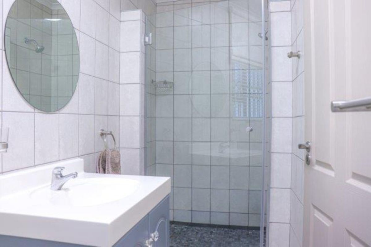 A clean, functional bathroom featuring a vanity with a basin, a glass-enclosed shower, and neutral wall tiling.