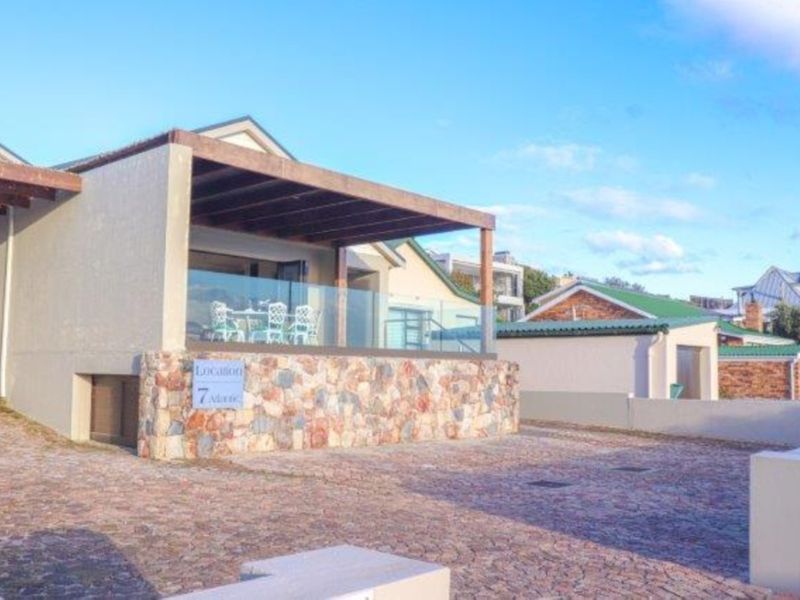 Front exterior view featuring a paved driveway, stone-clad base, and a covered patio area with a timber pergola and glass balustrade.