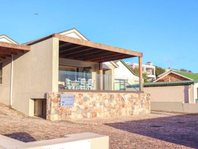 Front exterior view of the property featuring a stone-clad base, timber pergola, and glass balustrade overlooking a paved driveway.