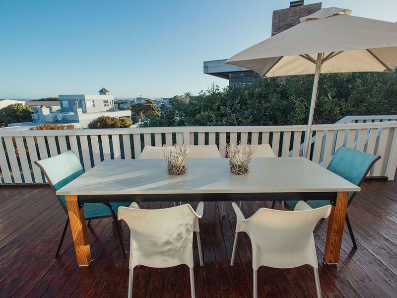 Elevated outdoor balcony featuring timber decking and a white balustrade, offering an open-air space for dining with neighborhood views.