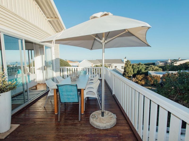 An elevated timber balcony featuring white balustrades and sliding glass door access, offering an outdoor space with coastal views.