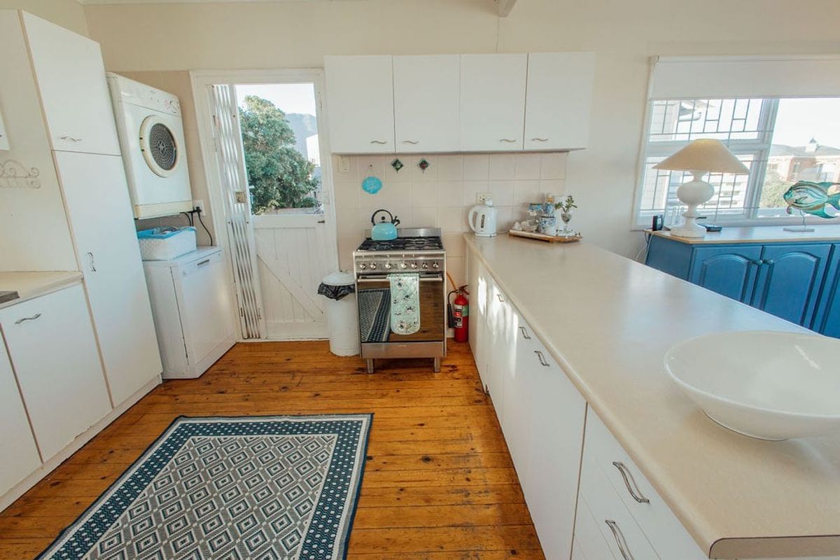 Functional kitchen featuring timber flooring, laminate countertops, built-in cabinetry, and a freestanding stove with direct access to the exterior.