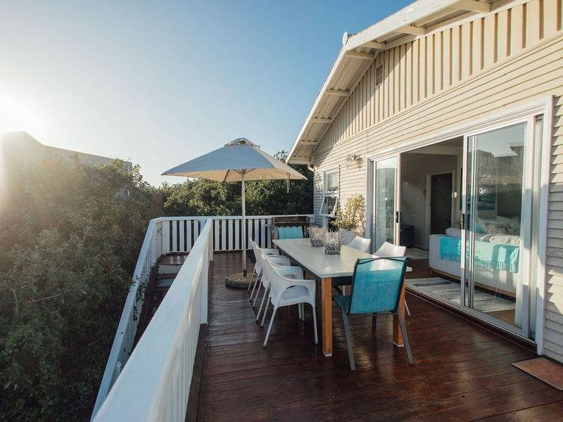 An elevated timber deck featuring white balustrades and sliding glass door access to the interior, providing a functional outdoor entertainment space.