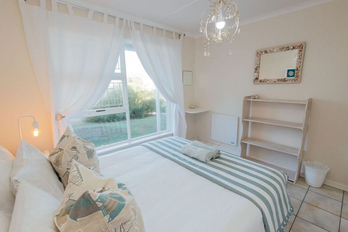 A bright bedroom featuring tiled flooring, a wall-mounted heater, and a large window providing natural light.