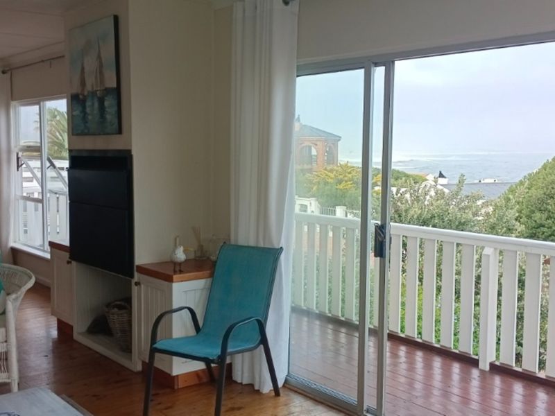 Living area featuring timber flooring, a built-in fireplace, and large sliding glass doors opening onto a balcony with coastal views.