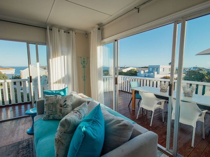 Bright living area featuring expansive sliding glass doors that open onto a wooden deck with coastal views.