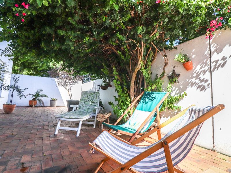 A private outdoor patio area featuring brick paving and a high boundary wall, shaded by a mature tree.