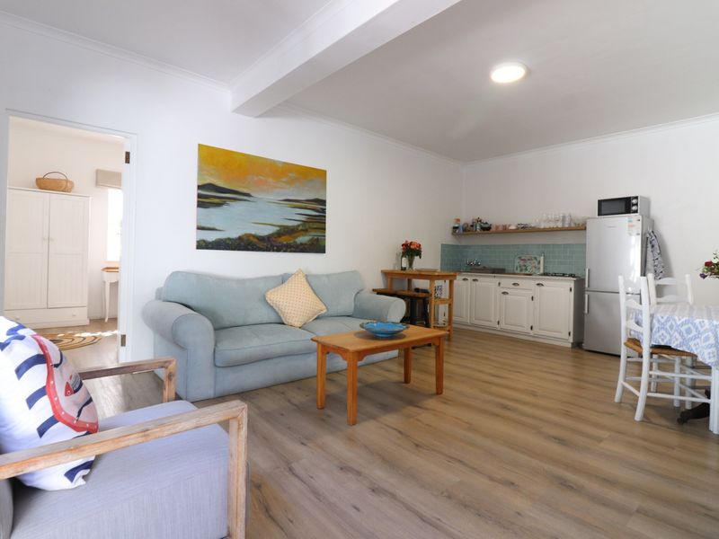 An open-plan living and kitchen area featuring light wood-look laminate flooring, white cabinetry, and a subway tile backsplash.