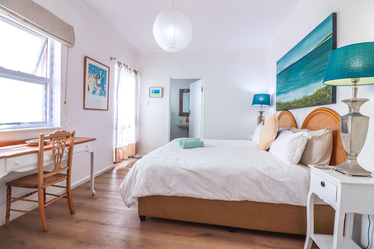 A bright and well-maintained bedroom featuring laminate flooring, a large casement window, and an en-suite bathroom access.