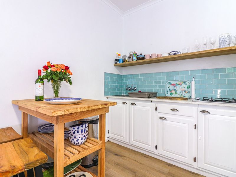 A compact kitchen featuring white cabinetry, a vibrant turquoise subway tile backsplash, a wooden floating shelf, and a gas cooktop.