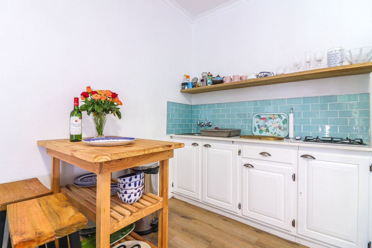 A compact kitchen featuring white cabinetry, a vibrant turquoise subway tile backsplash, a wooden floating shelf, and a gas cooktop.