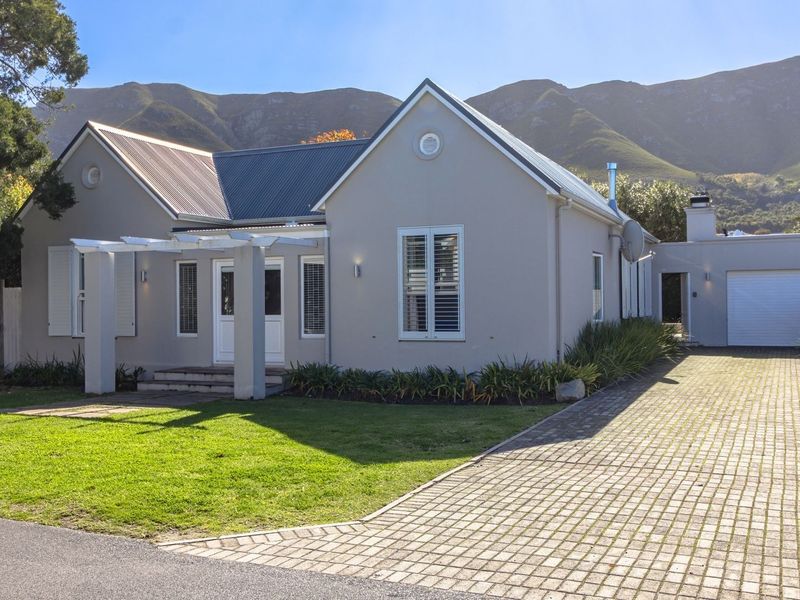 A well-maintained single-story house featuring a paved driveway, attached garage, pergola entrance, and mountain views in a quiet residential setting.