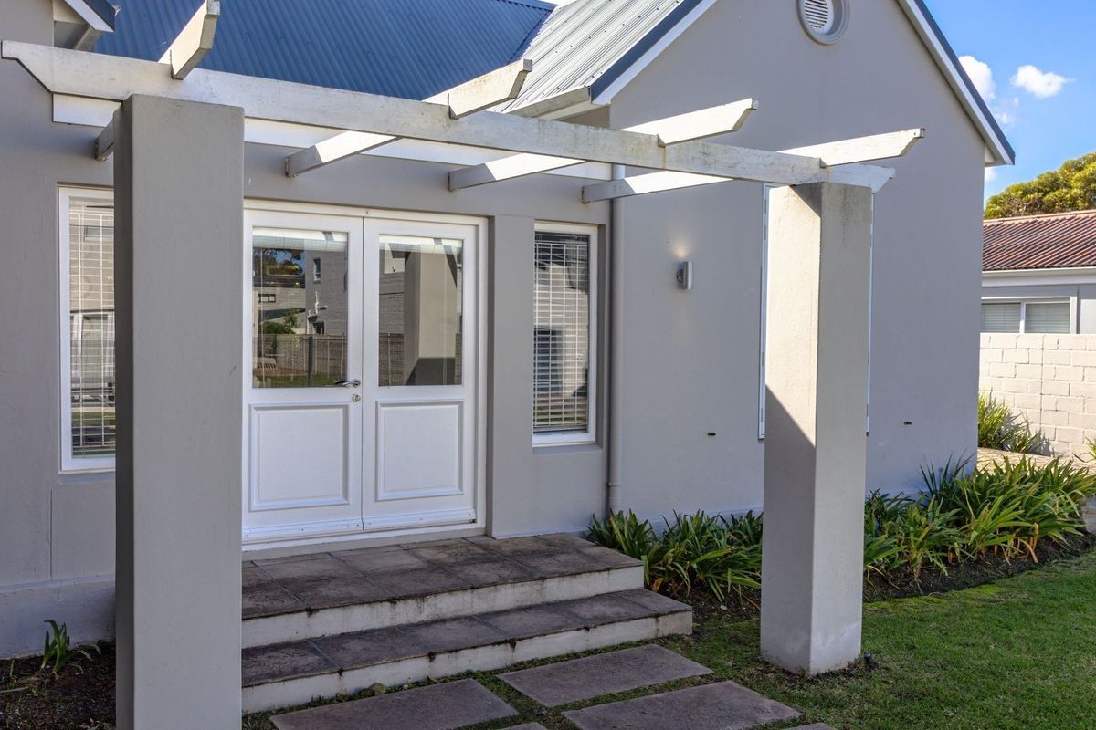 Rear exterior view featuring a paved patio area with a pergola structure, double glass doors, and well-maintained garden borders.