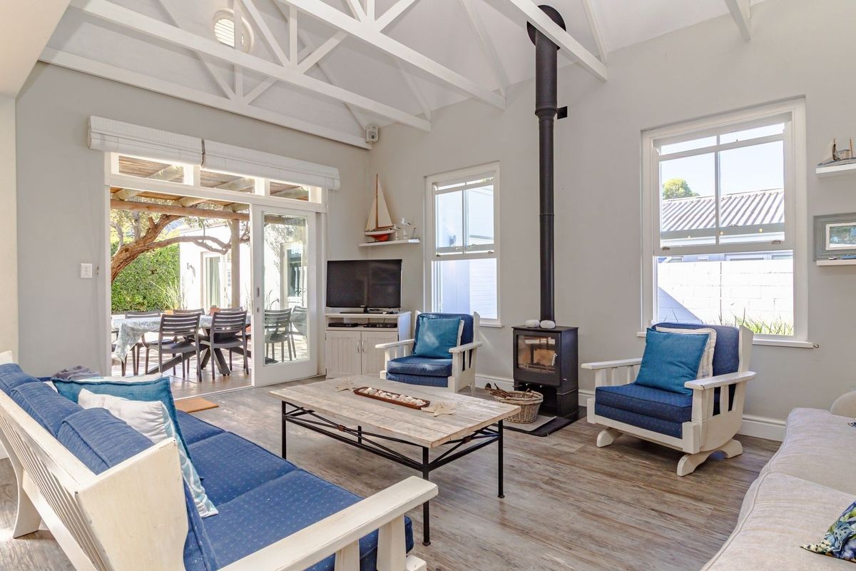 Bright living room featuring a vaulted ceiling with exposed trusses, a freestanding wood-burning fireplace, and sliding doors opening to an outdoor patio area.