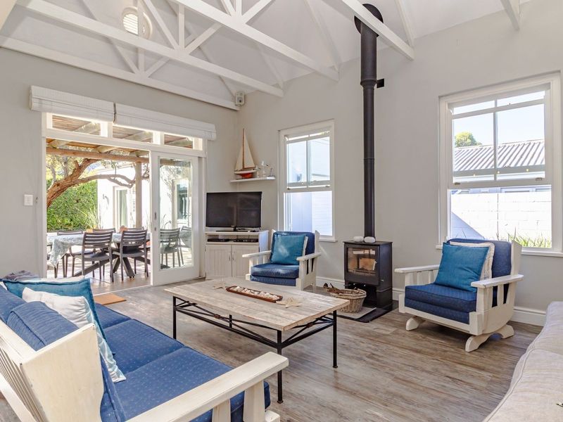 Bright living room featuring a vaulted ceiling with exposed trusses, a freestanding wood-burning fireplace, and sliding doors opening to an outdoor patio area.