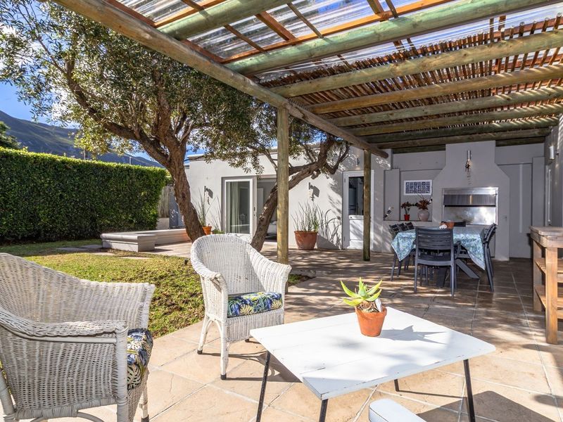 A spacious covered patio featuring a timber pergola and a built-in braai, overlooking a private garden with mountain views.