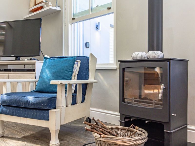 A cozy living room featuring a black wood-burning stove, sash window, and timber-look flooring.