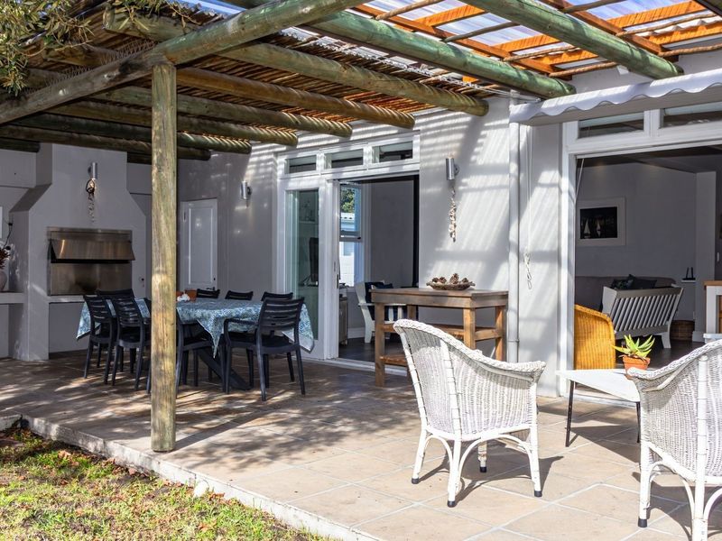 Covered outdoor patio featuring a timber pergola, tiled flooring, and a built-in braai, providing seamless indoor-outdoor flow through sliding glass doors.