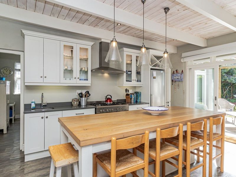 A bright, modern kitchen featuring shaker-style cabinetry, stone countertops, a stainless steel gas range, and exposed timber beam ceilings, opening directly to the garden.