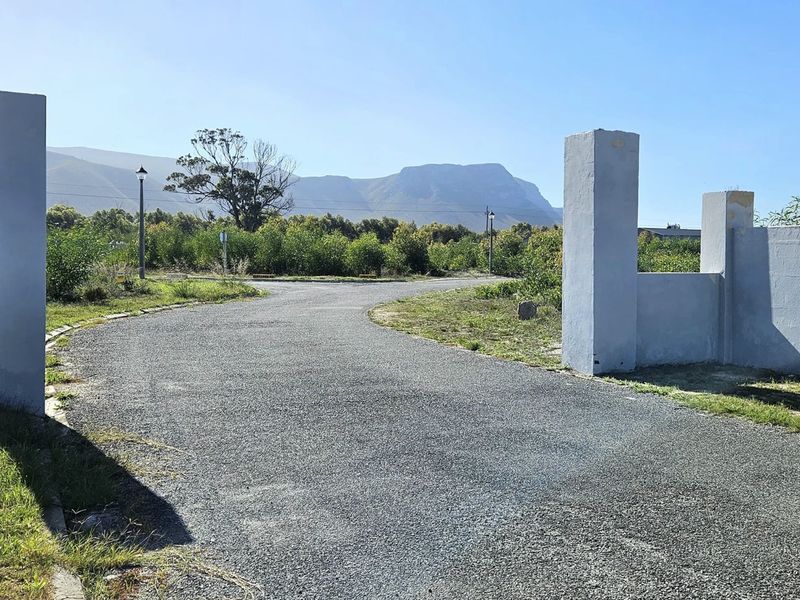 A view of the property entrance featuring masonry pillars, a paved driveway, and surrounding landscape with mountain views.