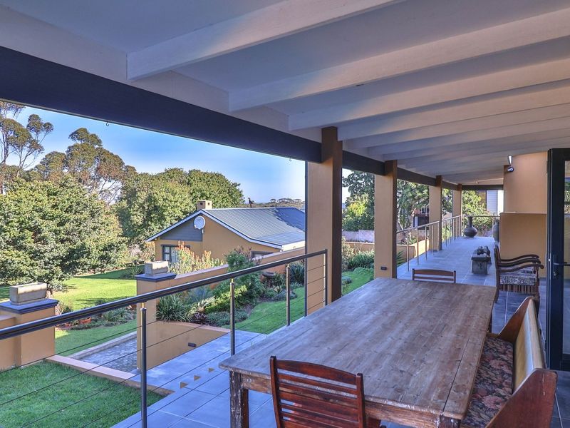 Spacious covered patio featuring tiled flooring, exposed beam ceiling, and stainless steel cable railings, overlooking a landscaped garden and surrounding neighborhood.