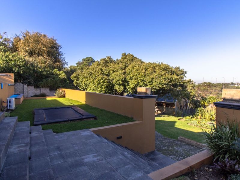 A well-maintained rear garden featuring tiered stone stairs, retaining walls, and a spacious lawn area with established landscaping.