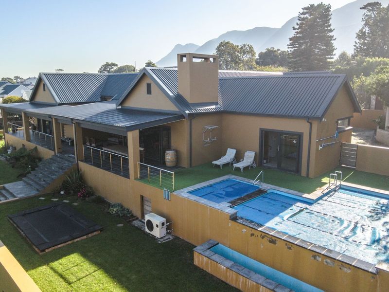 Aerial view of a residential property featuring a swimming pool, covered patio area, metal roofing, and landscaped garden with mountain views.
