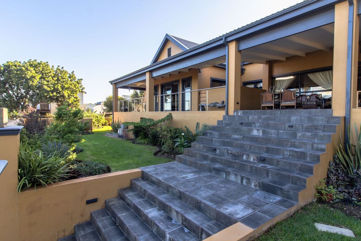 Spacious rear exterior featuring a covered patio, stone staircase with stainless steel railings, and a well-maintained landscaped garden.