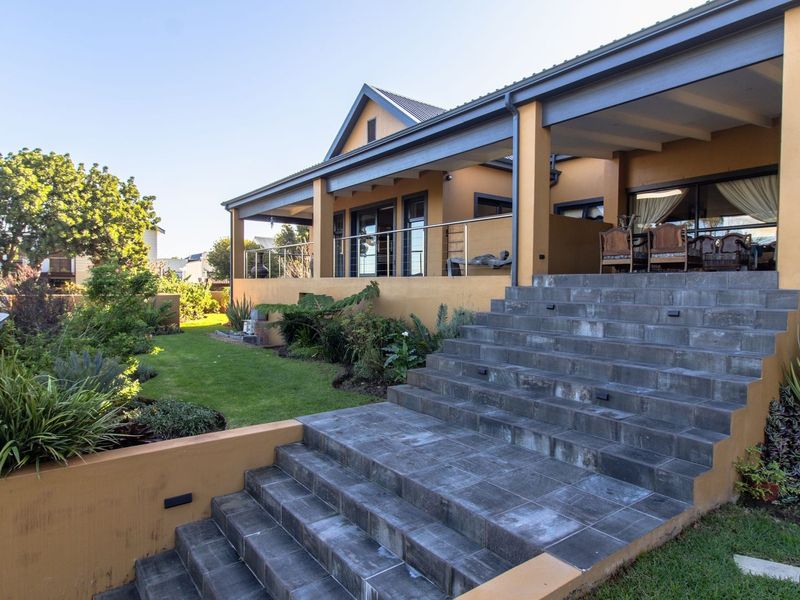 Spacious rear exterior featuring a covered patio, stone staircase with stainless steel railings, and a well-maintained landscaped garden.