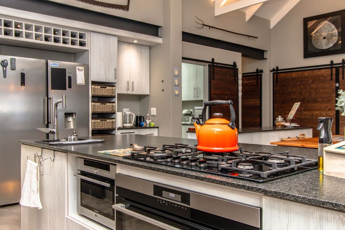 Modern kitchen featuring a large island with a gas cooktop, built-in oven, stone countertops, and stylish barn-style sliding doors leading to adjacent spaces.