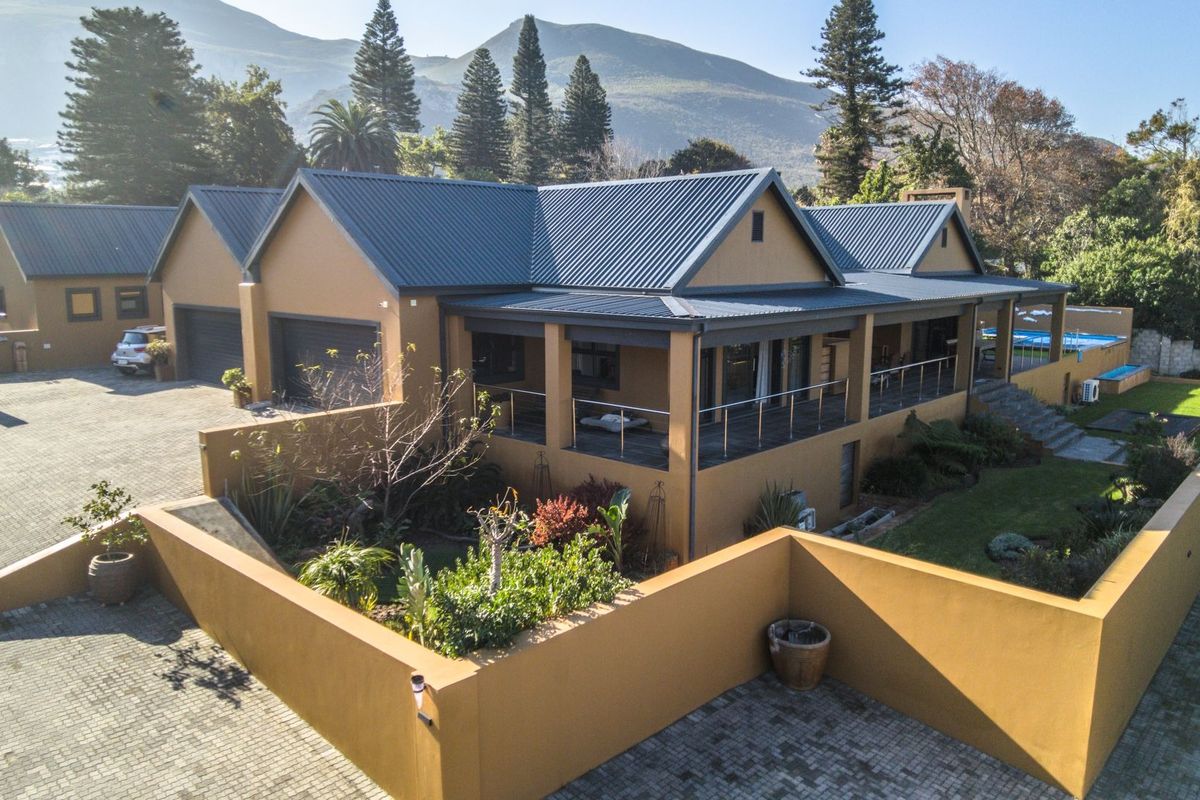 Aerial view of a well-maintained residential property featuring a metal roof, paved driveway, double garage, and a spacious covered patio overlooking the garden.