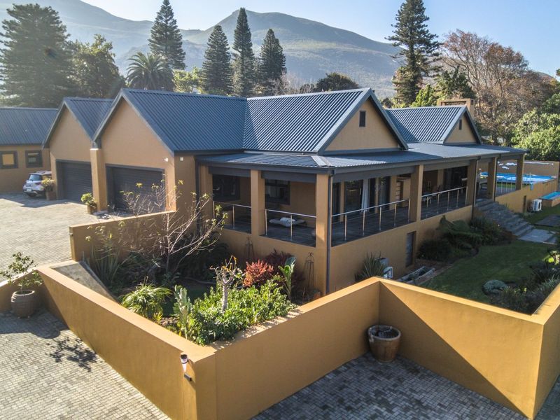 Aerial view of a well-maintained residential property featuring a metal roof, paved driveway, double garage, and a spacious covered patio overlooking the garden.