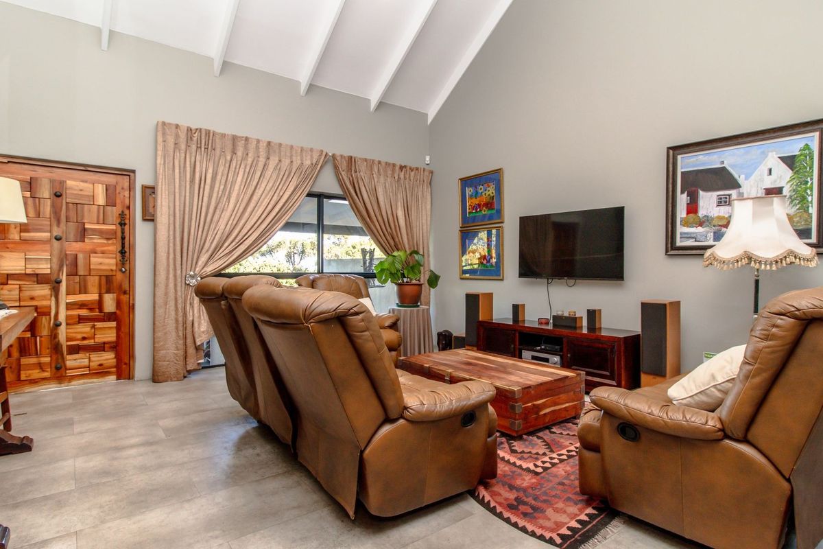 Spacious living room featuring a high vaulted ceiling with exposed rafters, neutral wall finishes, tiled flooring, and a distinctive solid wood entrance door.