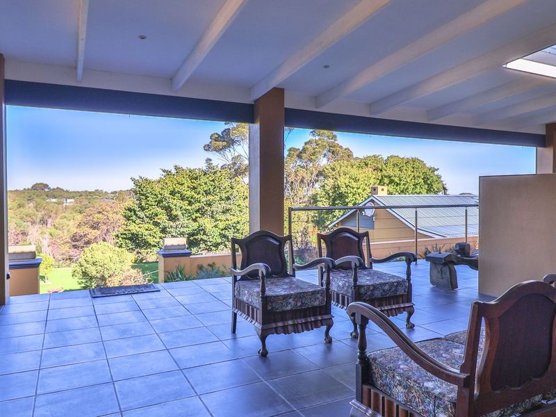 A spacious covered patio featuring tiled flooring, exposed beam ceilings, and a glass balustrade, offering expansive views of the surrounding landscape.